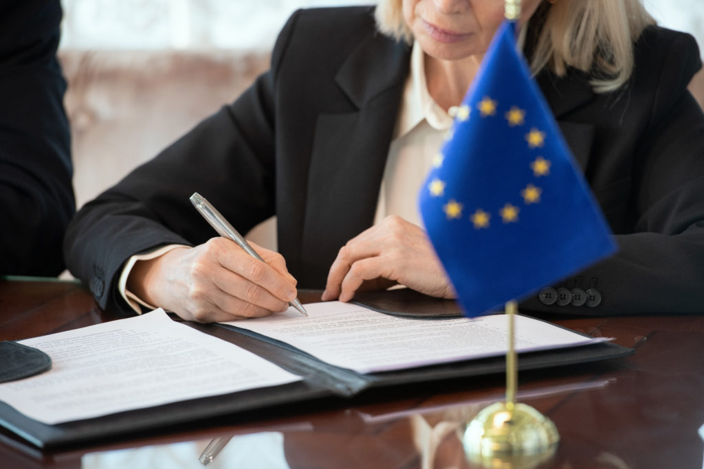 Flag of European Union on table against mature female delegate signing contract